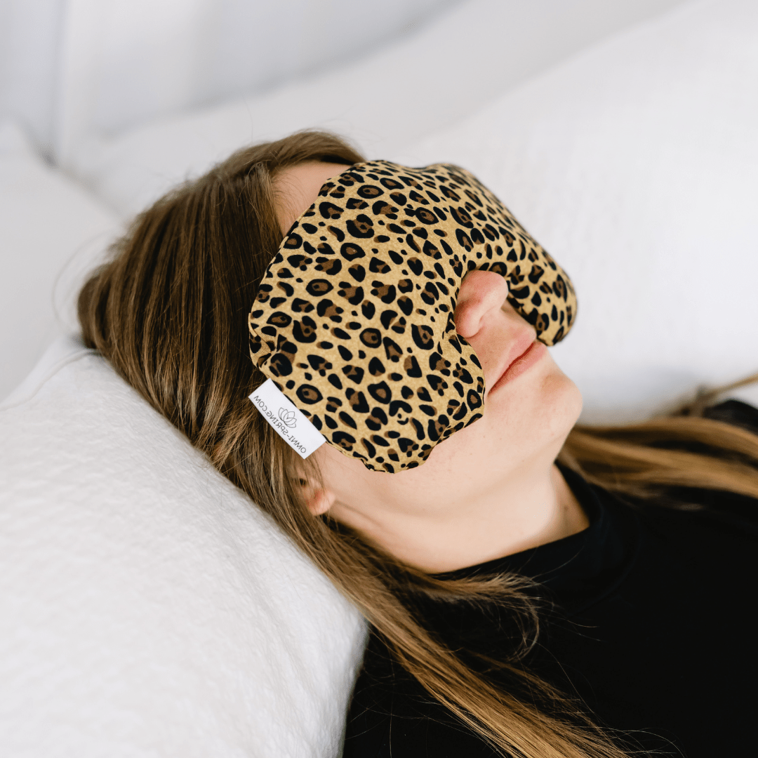 A person lying down wearing a contoured eye pillow with a leopard print design.