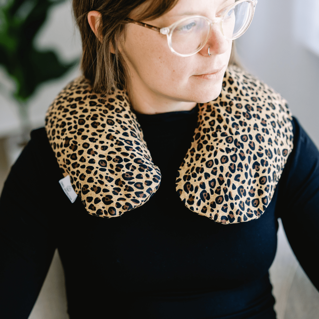A person wearing a leopard print U-shaped pillow around the neck.